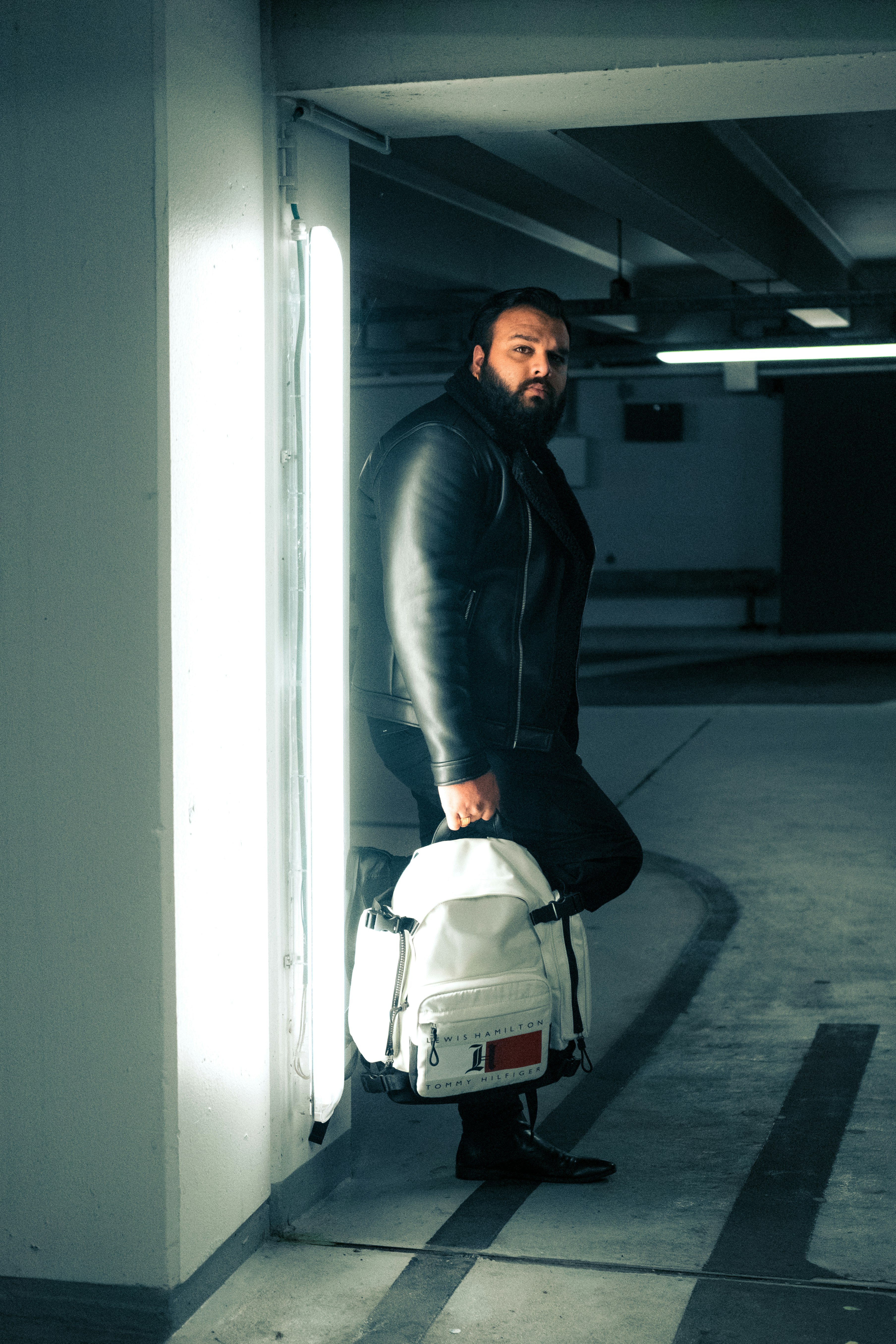 man in black leather jacket and gray pants holding white and black backpack